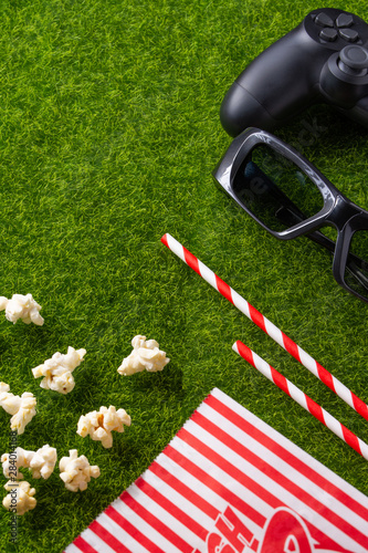 Packing with popcorn straws for soda on a green lawn with a joystick for games and with 3D glasses for watching a movie. Grass Watching films about nature. In parks. Recreation and entertainment