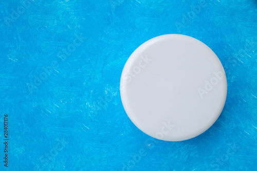 Top view round white plastic cream jar on a blue background.