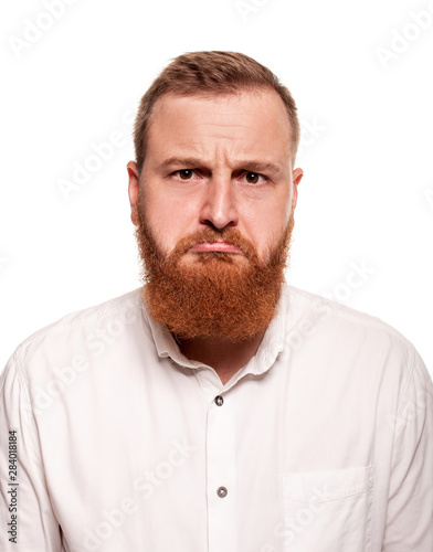 Portrait of a young, chubby, redheaded man in a white shirt making faces at the camera, isolated on a white background