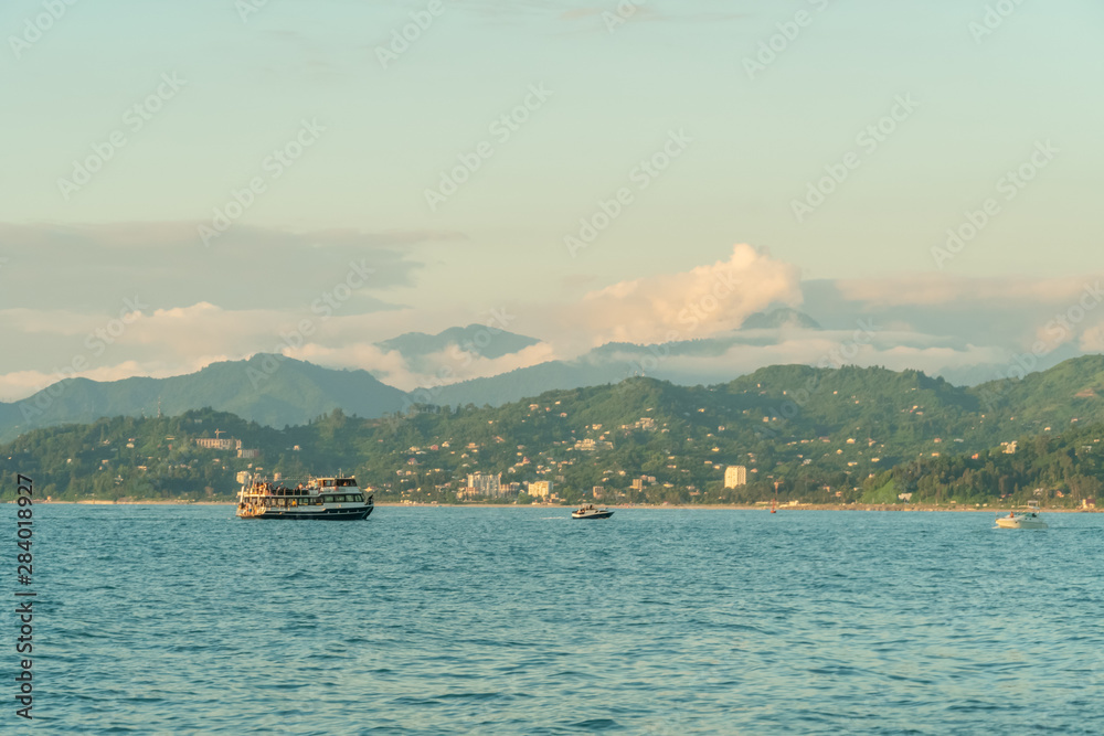 Small pleasure tourist boat floating from the port for a cruise off the coast on a Sunny summer evening against the background of the mountains, Batumi