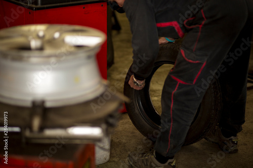 Man changing car tires in garage because of winter season. Workplace environment in dark colors, fitting the tire on rim.