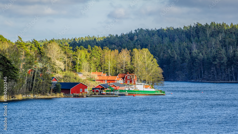 Φωτογραφία Small idyllic port in the swedish archipelago outside of Stockholm with moored coastal ro-ro ferry and earthmovers lighted with sunspot