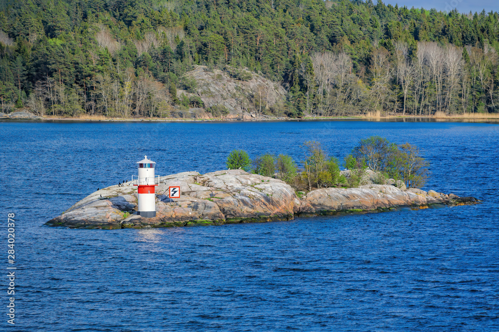 Φωτογραφία Beacon or small lighthouse in red and white at a rocky shore of Oxdjupet strait during the evening with coniferous forest and islands on the background