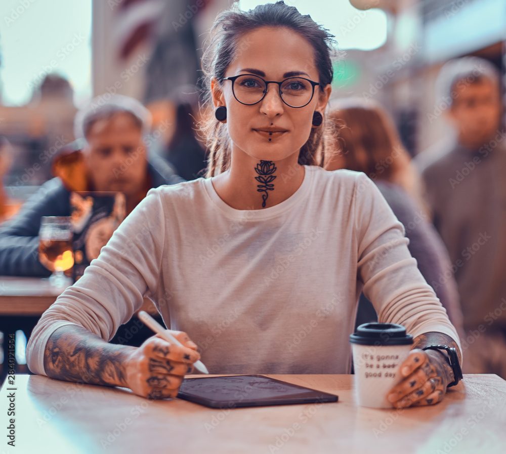 Φωτογραφία Young pretty woman with tattooes on her hands is enjoying her time at food court with her sketching pad