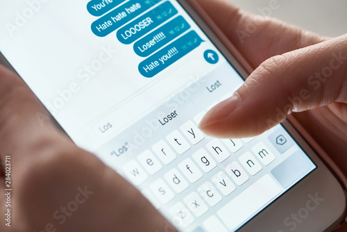 close up view of abuser sending offensive messages while using smartphone, illustrative editorial