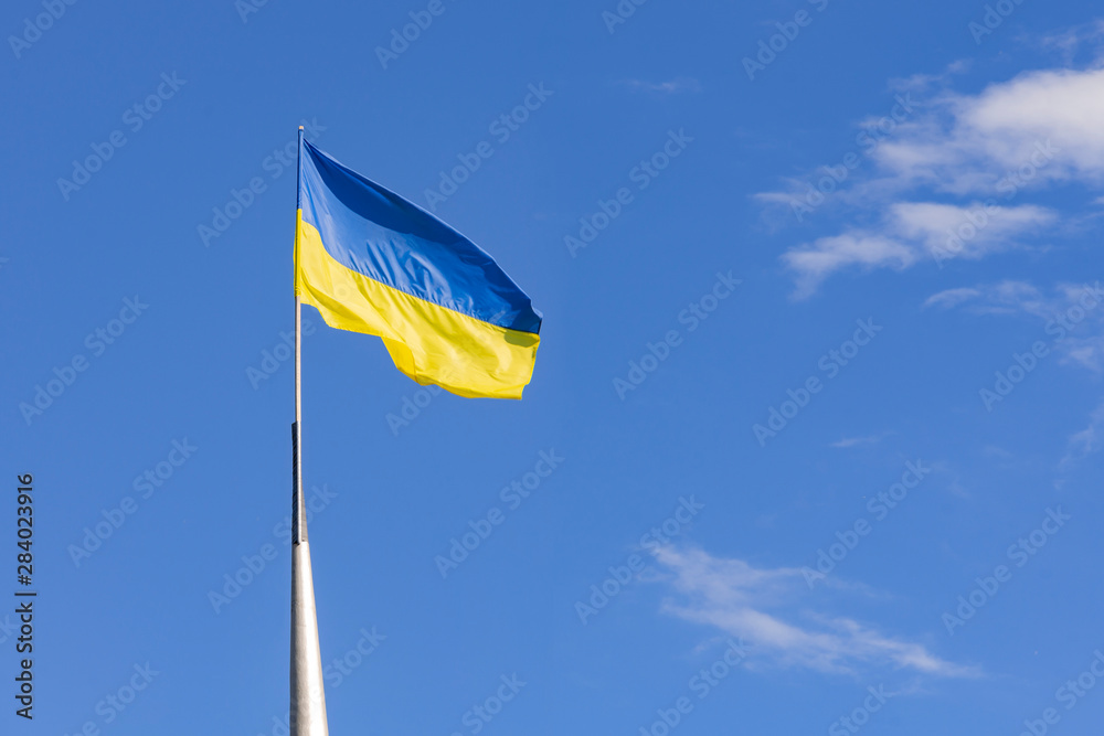 Waving flag of Ukraine on the street flagpole with blue cloudy sky on background. Ukrainian country symbol Waving flag of Ukraine on the street flagpole with blue cloudy sky on background. Ukrainian country symbol