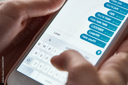 partial view of abuser sending offensive messages while using smartphone, illustrative editorial