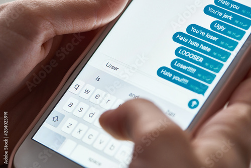 partial view of abuser sending offensive messages while using smartphone, illustrative editorial photo