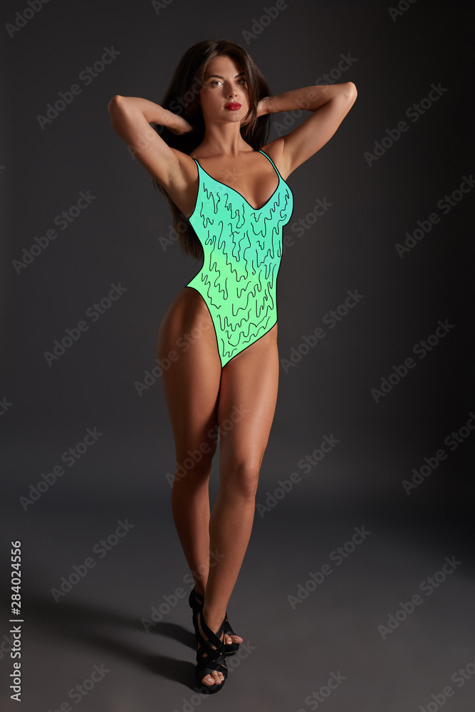 Full-length portrait of a brunette sexy woman in a cartoon colorful swimwear posing against a black background.