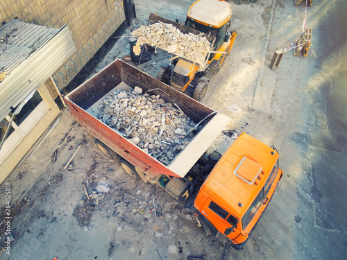 Bulldozer loader uploading waste and debris into dump truck at construction site. building dismantling and construction waste disposal service. Aerial drone industrial background photo