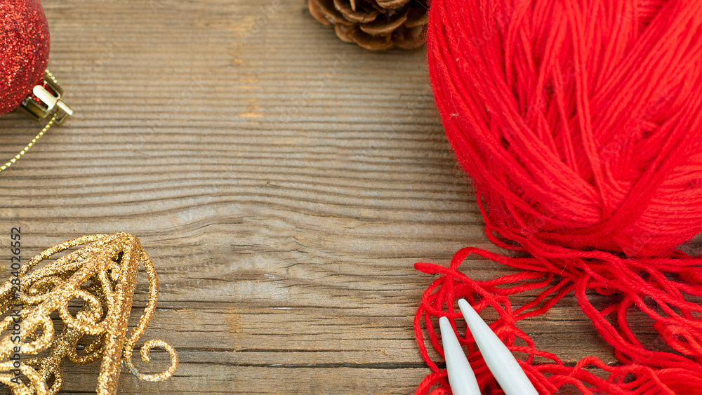 knitting sticks red yarn and christmas decoration on old textured wooden background. Horizontal banner with copy space. Clew ball with accessories, winter gift, present for handwork knitting sticks red yarn and christmas decoration on old textured wooden background. Horizontal banner with copy space. Clew ball with accessories, winter gift, present for handwork