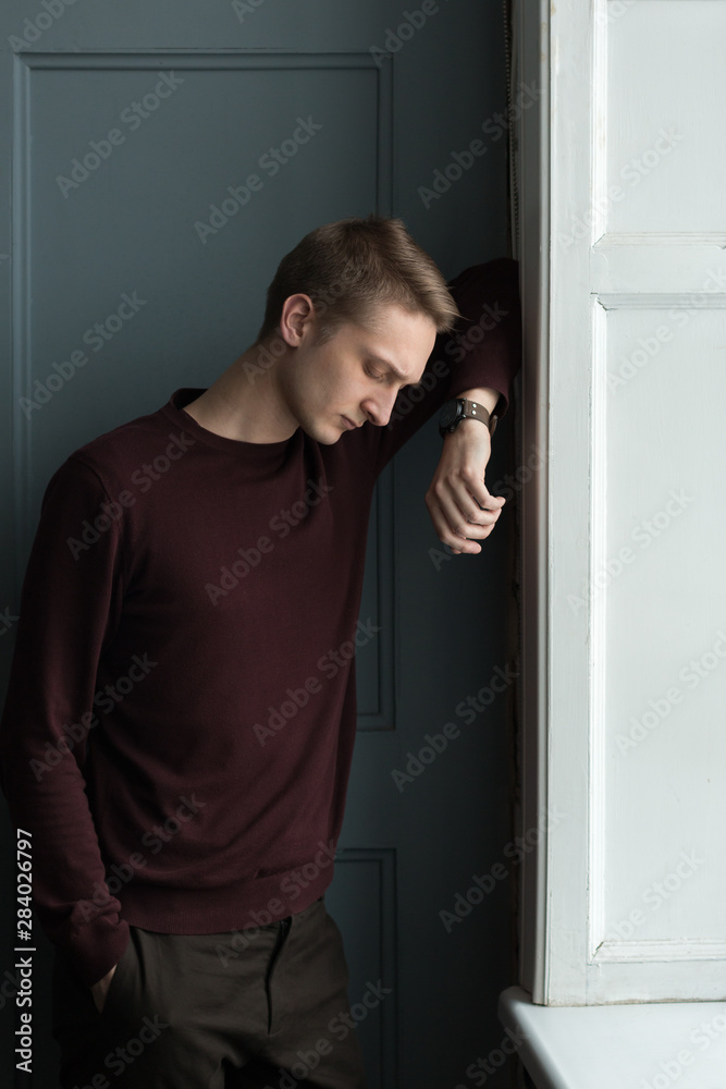 Sad and thoughtful young guy standing at the window. Beautiful, expressive portrait made in the Studio in vintage style. Sad and thoughtful young guy standing at the window. Beautiful, expressive portrait made in the Studio in vintage style.