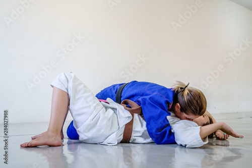 Side control 100 kilos position, americana submission judo bjj brazilian jiu-jitsu training sparring two women female fighters in training wearing kimono