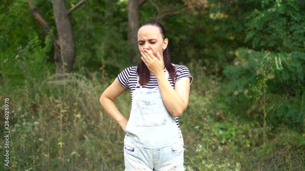 A beautiful young woman in casual clothes yawns from fatigue in the forest. A beautiful young woman in casual clothes yawns from fatigue in the forest.