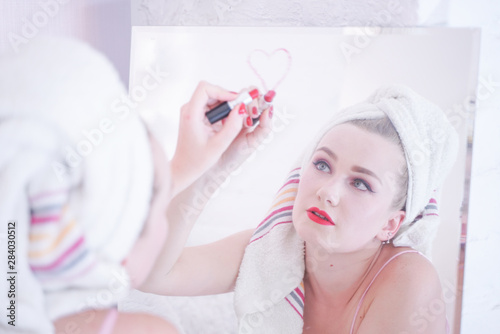 Attractive Young Woman Wrapped with Bath Towel After a Shower at the Bathroom near the mirror with lipstick photo