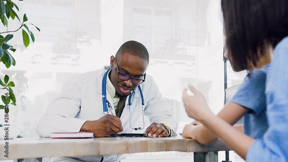 African young doctor giving prescription to cute mother with here son at clinic. African young doctor giving prescription to cute mother with here son at clinic.