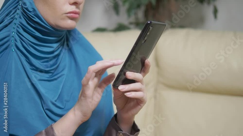 beautiful muslim woman in blue hijab using a mobile phone sitting on a sofa photo