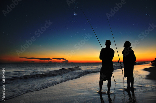 Dos hombres pescando al atardecer con un cielo estrellado