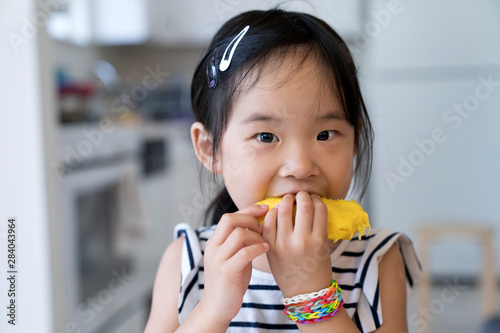 Happy cute little Asian girl eating mango with funny face