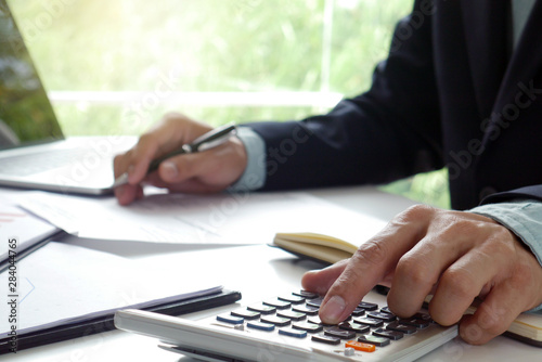 Men use the calculator and take notes with calculations about the expenses at the office. Prepare to submit annual tax