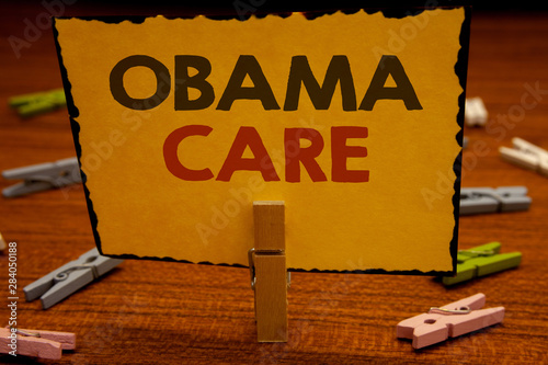 Words writing texts Obama Care. Business concept for Government Program of Insurance System Patient ProtectionClothespin hold holding Yellow paper ideas clothespins wooden background