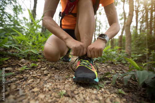 Woman ultra marathon runner tying shoelace on rainforest trail