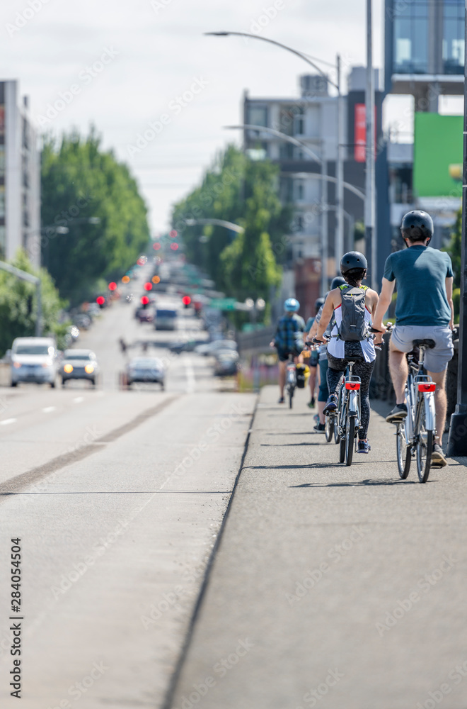 String of cyclists rides on the sidewalk of a city street