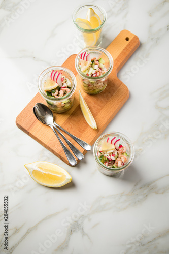 Norddeutscher Friesischer Nordseekrabben Salat Glas Becher mit Gurken, Radieschen, Zwiebeln, Dill und Zitronen auf Holz Brett und Marmor Tisch photo