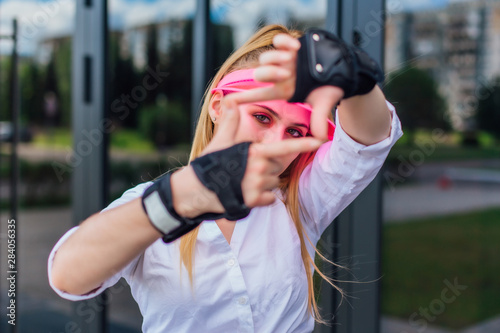 Portrait of an emotional girl in a pink cap visor and protective gloves for rollerblades and skateboarding making a frame. © Smile
