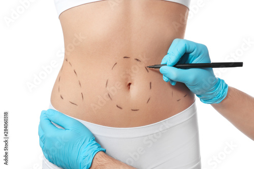 Doctor drawing marks on woman's body for cosmetic surgery operation against white background, closeup