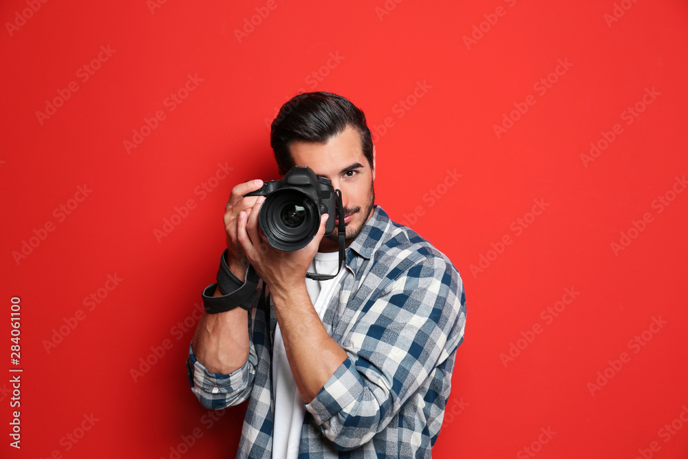 Young professional photographer taking picture on red background - obrazy, fototapety, plakaty 