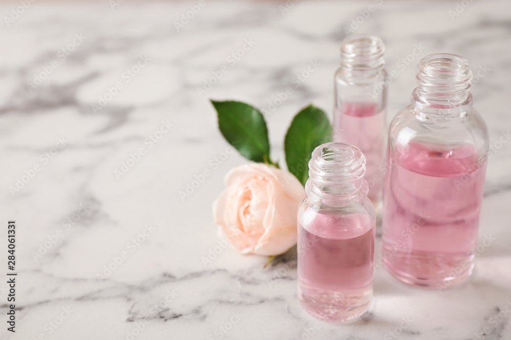 Bottles of essential oil and rose on marble table. Space for text Bottles of essential oil and rose on marble table. Space for text