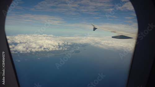 Aircraft porthole with blue sea or ocean and tropical islands. Looking through window aircraft during flight. Airplane wing through the porthole. Looking through window aircraft during flight © Alex Traveler