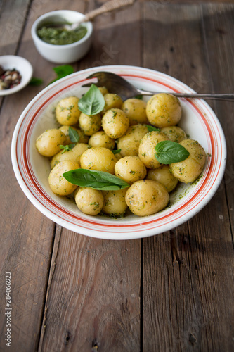 Potato. Tasty Young boiled potatoes with basil in white bowl on rustic wooden table.