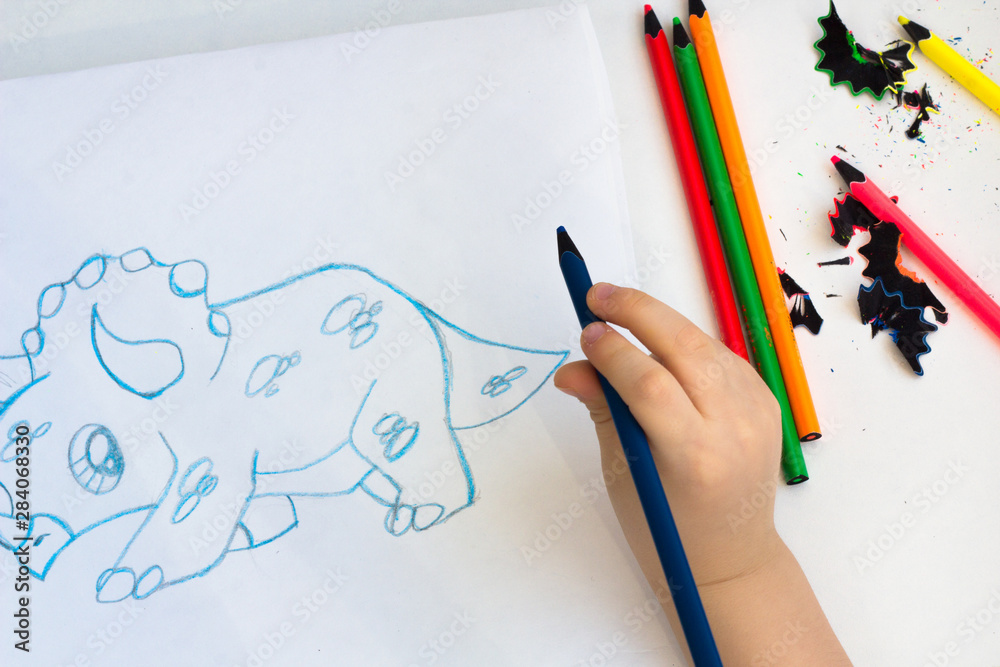 A child draws a dinosaur with a color pencil. A child draws a dinosaur with a color pencil.