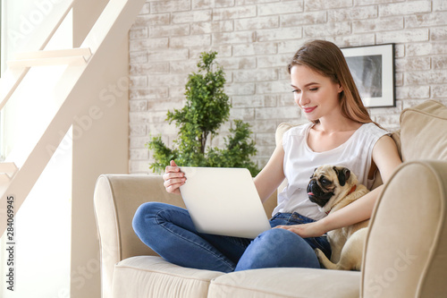 Beautiful young woman with cute pug dog working on laptop at home