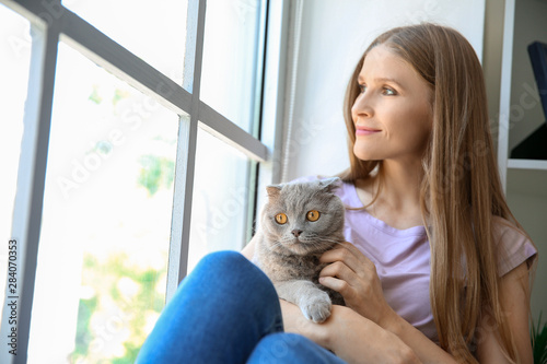Beautiful woman with cute cat sitting near window © Pixel-Shot