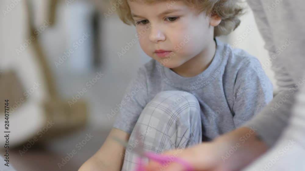 Tilt up shot of cute blonde boy cutting paper with scissors and listening to mom while making Christmas crafts together at home Tilt up shot of cute blonde boy cutting paper with scissors and listening to mom while making Christmas crafts together at home