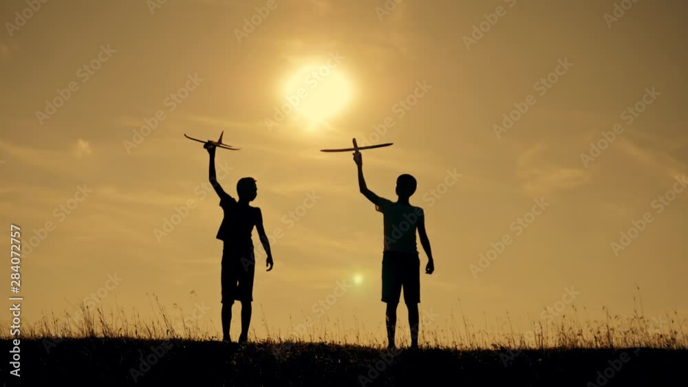 Two boys play with a wooden plane at sunset. Silhouette of children ...
