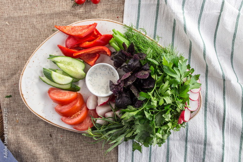 Plate with fresh vegetable sliced salad with cucumber, tomato, pepper and basil, parsley and cream sauce on tablelcoth photo