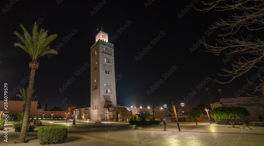 Koutoubia Mosque in city center with narrow street and traditional houses and people, muslim architecture,.