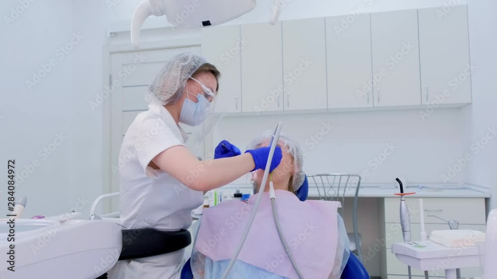 Dental hygienist cleaning and brushing woman's teeth uses drill with