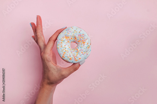 Woman s hand holding a donut with colorful sprinkles on pink background