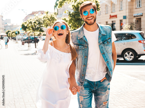 Smiling beautiful girl and her handsome boyfriend posing in the street. Woman in casual summer dress and man in jeans clothes. Happy cheerful couple family having fun in sunglasses