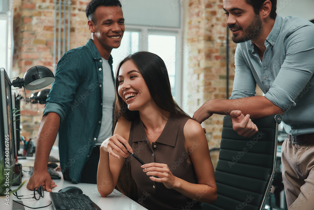 Perfect teamwork. Group of young and cheerful three people discussing new ideas and smiling while working in modern office Perfect teamwork. Group of young and cheerful three people discussing new ideas and smiling while working in modern office