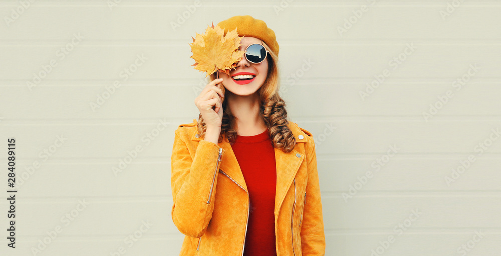 Autumn mood! happy smiling woman holding in her hands yellow maple leaves hiding her eye over gray wall background - obrazy, fototapety, plakaty 