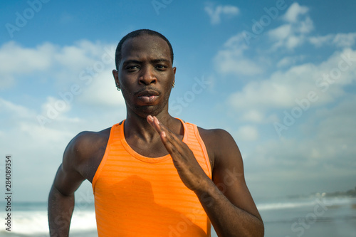 athletic full body portrait of young attractive and fit black afro American man running on the beach doing Summer fitness jogging workout at the sea in healthy lifestyle concept