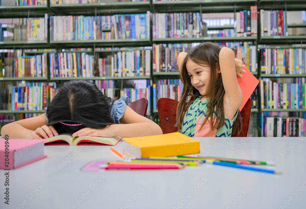 Happiness two cute diversity girls reading book and teasing to hit sleeping friend in school library funny. People lifestyle and Education and friendship. Child and kids group activity leisure Happiness two cute diversity girls reading book and teasing to hit sleeping friend in school library funny. People lifestyle and Education and friendship. Child and kids group activity leisure