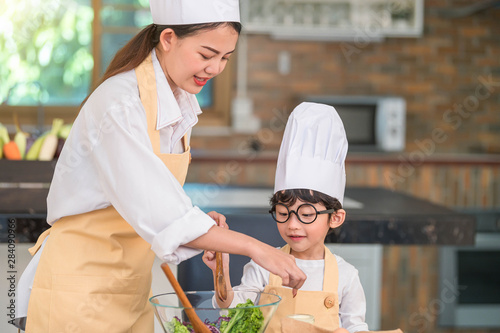 Happy beautiful Asian woman and cute little boy with eyeglasses prepare to cooking in kitchen at home. People lifestyles and Family. Homemade food and ingredients concept. Two Thai people life