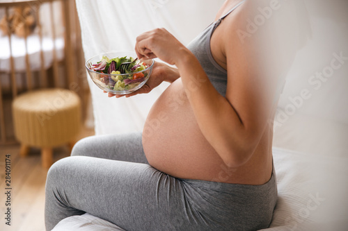 Pregnant lady eating fresh vegetable salad at home